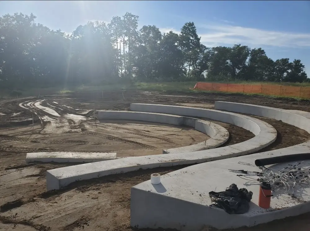 Curved poured-concrete retaining walls under sun-flared Minnesota tree line